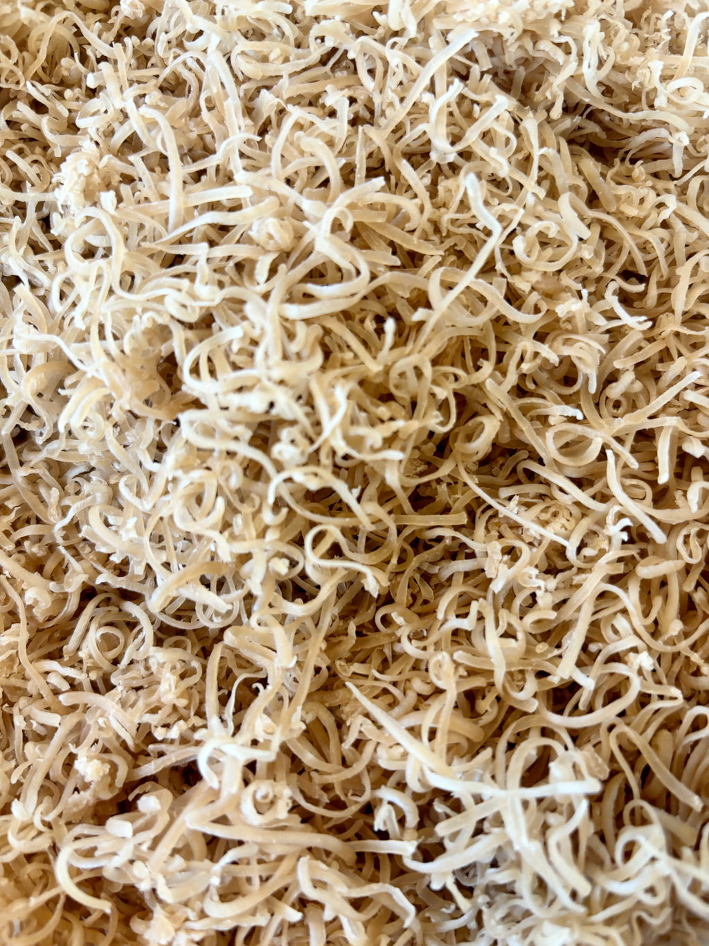 A close-up view of a dense pile of dried, curly, and twisted pale beige Milk Bath