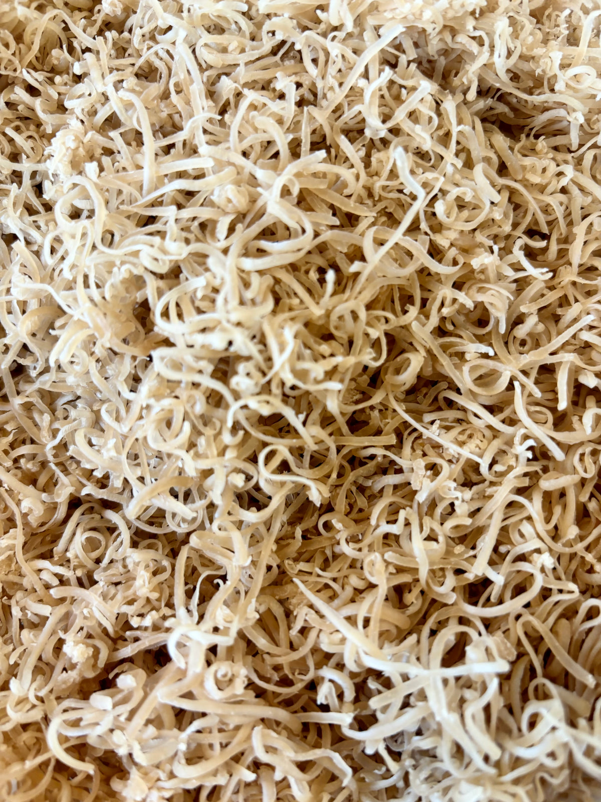 A close-up view of a dense pile of dried, curly, and twisted pale beige Milk Bath