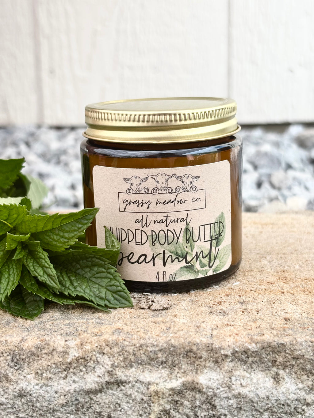 A jar of Grassy Meadow Co. All Natural Whipped Tallow (spearmint) sits on a stone surface next to fresh green mint leaves.